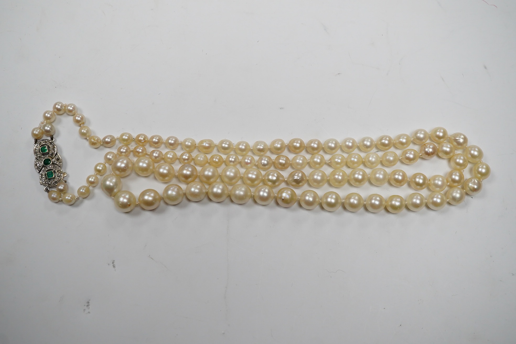 A single strand cultured pearl necklace, with and emerald and diamond cluster set white metal clasp, 76cm. Condition - fair.